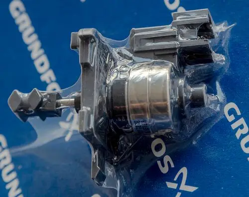 Daikin Schrittmotor in transparenter Verpackung, montiert auf blauem Hintergrund mit Logo. Sichtbare Anschlüsse an der Oberseite und ein metallischer Zylinder im Zentrum.